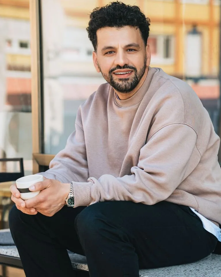 Mohamed „Mo“ Missbah sitzt mit einer Tasse vor dem Schaufenster des Coffee Lab und lächelt in die Kamera